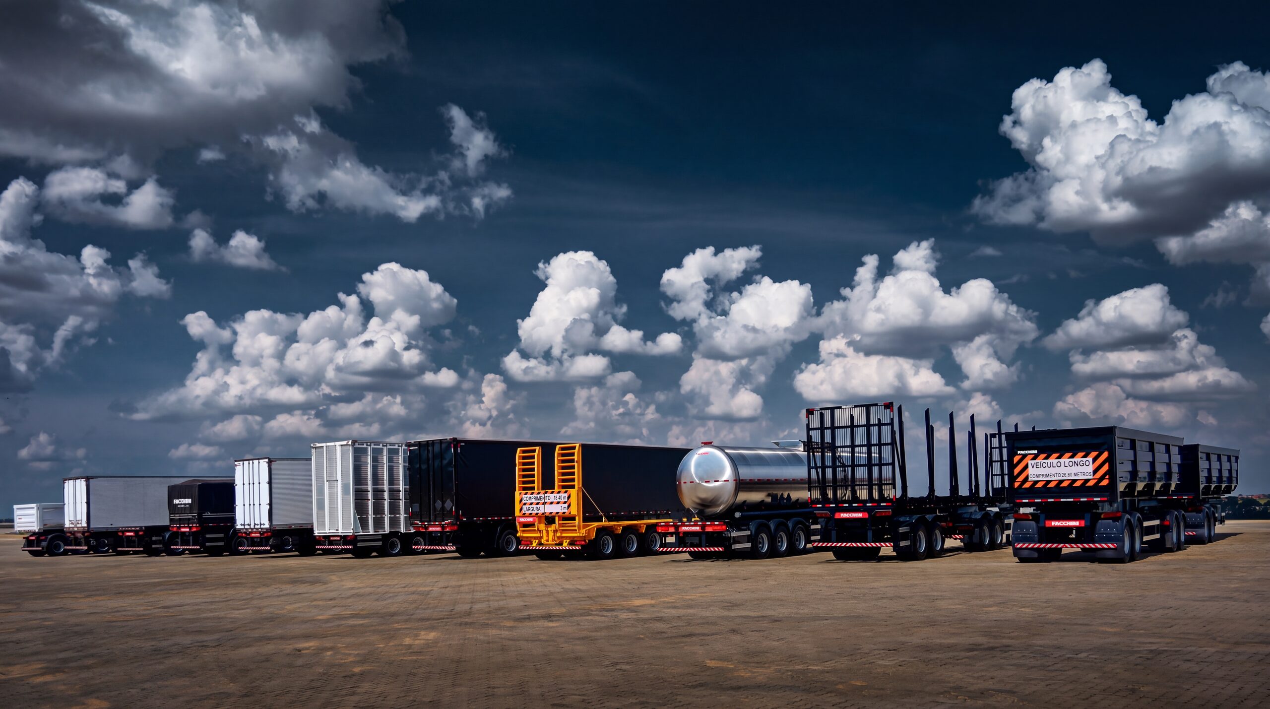 Linha completa de implementos rodoviários Facchini perfilada em pátio sob céu azul com nuvens: furgões, sider, prancha, tanque inox, florestal e bitrem basculante